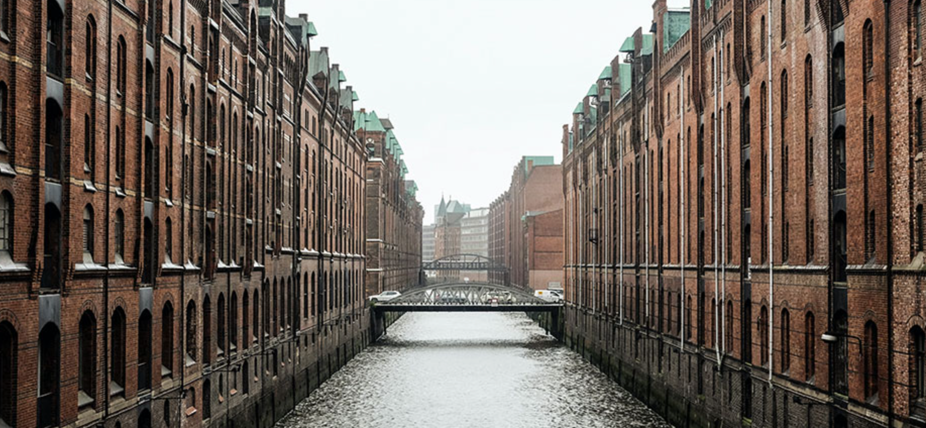 Backstein-Gebäude mit grünem Dach entlang eines Kanals, grauer Himmel.