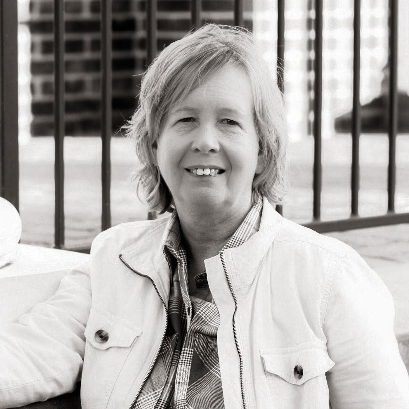 Frau in heller Jacke sitzt draußen, lächelt entspannt.