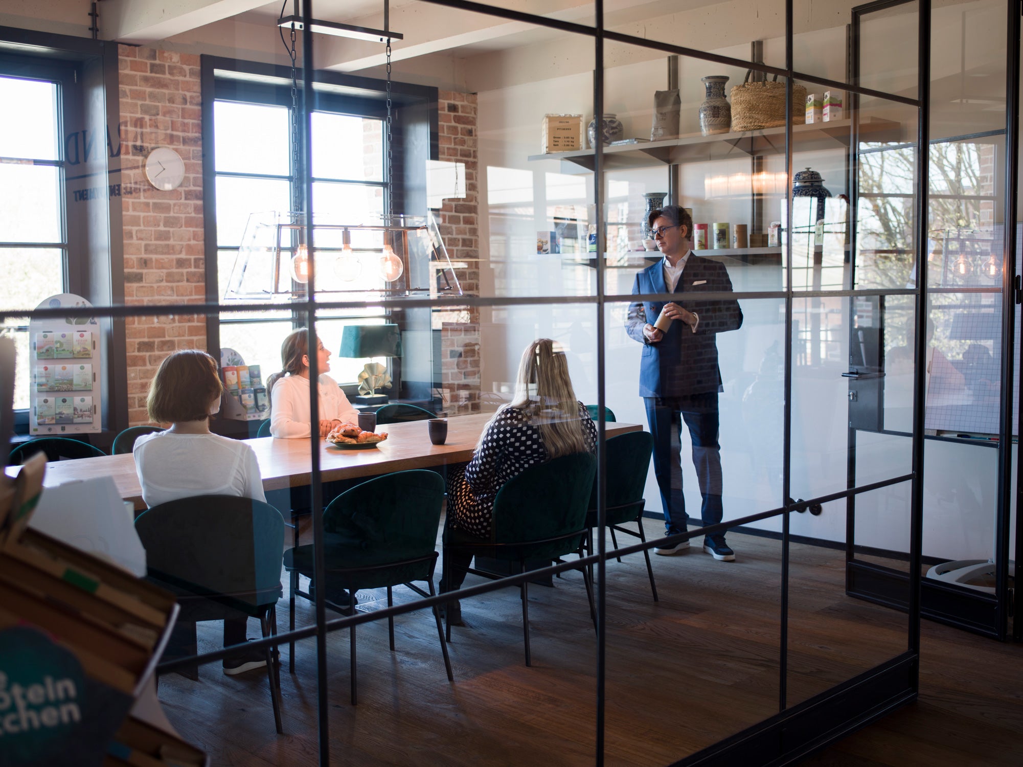 Mann steht vor sitzenden Menschen in einem Konferenzraum mit gläsernen Wänden.