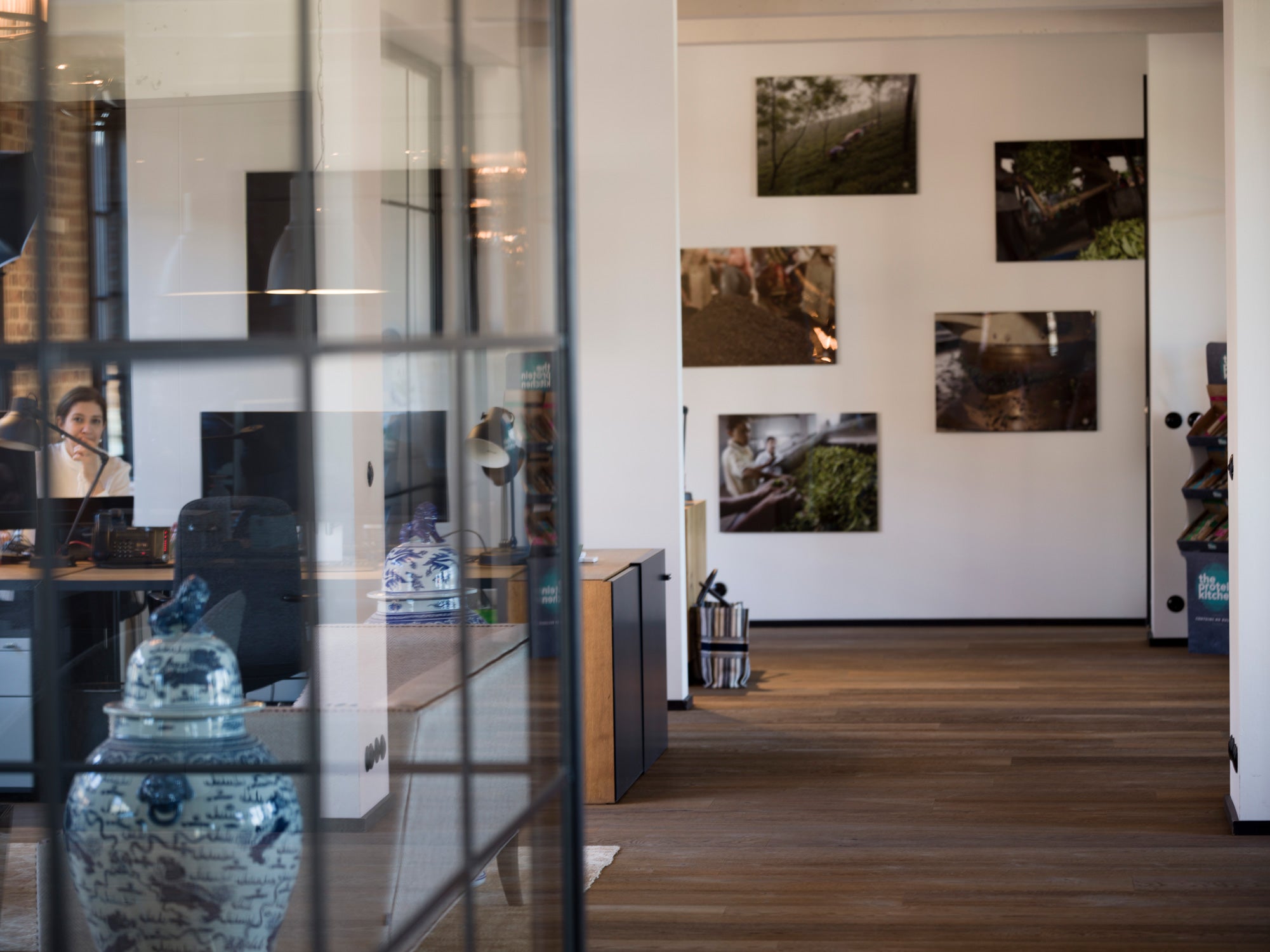 Moderner Büroraum mit Holzboden, durch Glaswände teilweise sichtbar, Bilder an der Wand.