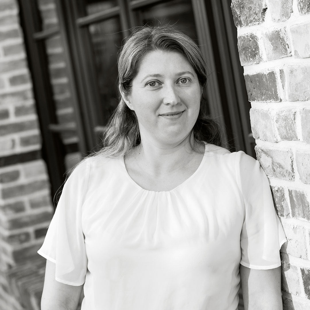 Frau mit langen Haaren in einem weißen Oberteil blickt freundlich in die Kamera.