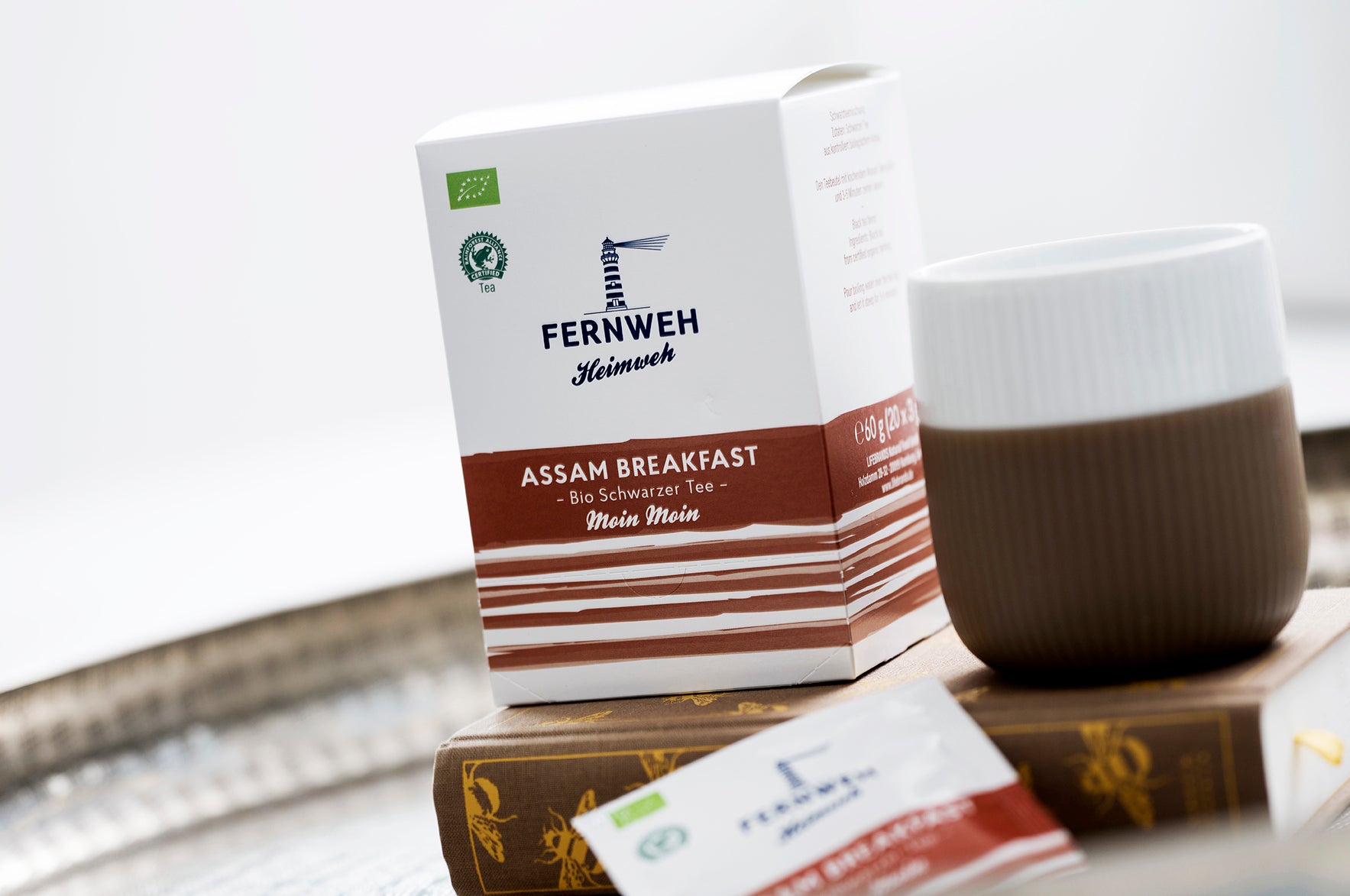 Teepackung Assam Breakfast mit weiß-brauner Tasse auf Tablett.