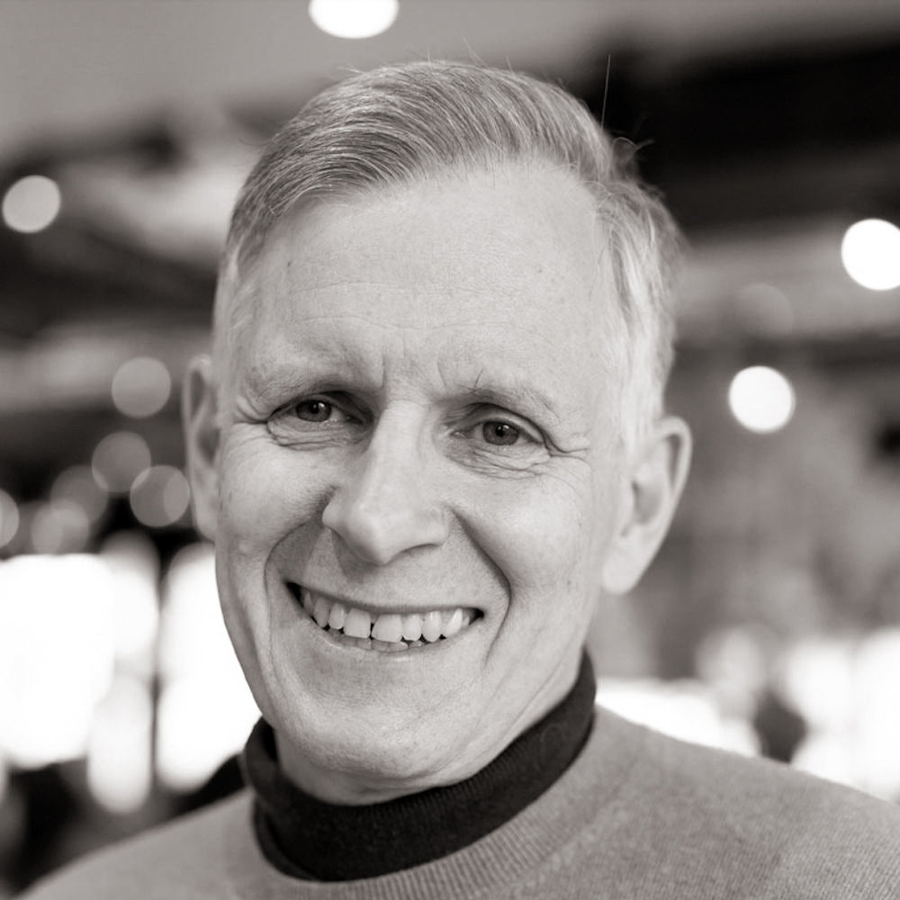 Lächelnder Mann mit grauem Haar in Schwarz-Weiß.